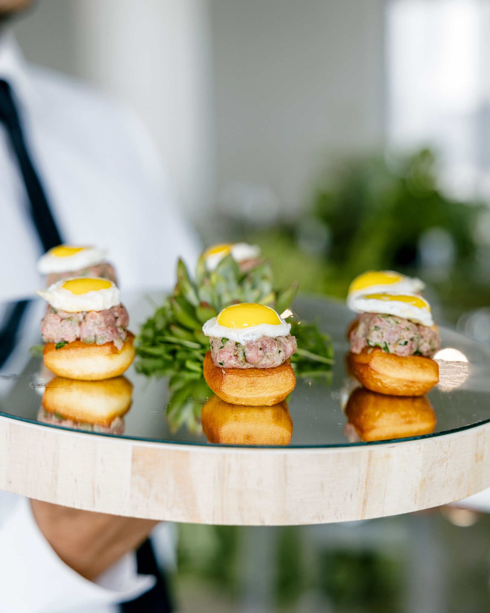 Beef tartare canapés topped with quail eggs on mirror tray